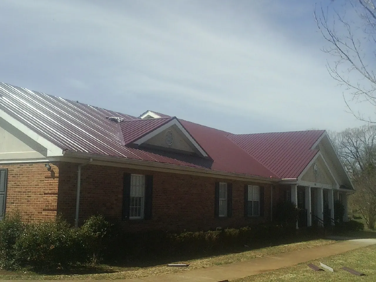 Red metal roof with gabled entries on a long brick building, from a Hail Damage Roof Repair job in Overton