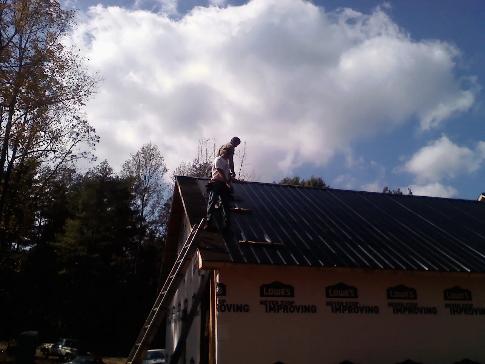 Roofer fastening dark metal panels high against a cloudy sky, from a Roof Inspection job in Overton