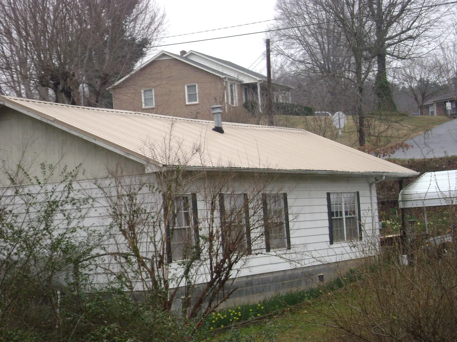 Tan metal roof on a white sided house set into a hillside — Commercial Roofing by Roofing Brothers in Overton